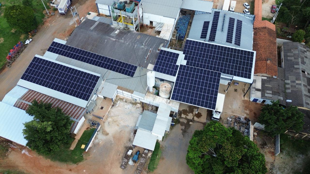 Vista aérea de um complexo industrial com módulos fotovoltaicos instalados sobre os telhados dos galpões.