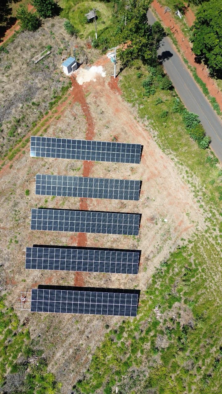 Vista aérea de uma usina fotovoltaica de solo com cinco fileiras de módulos em terreno rural.