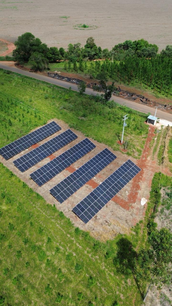 Vista aérea de uma usina fotovoltaica de solo instalada entre vegetação e área de plantio.